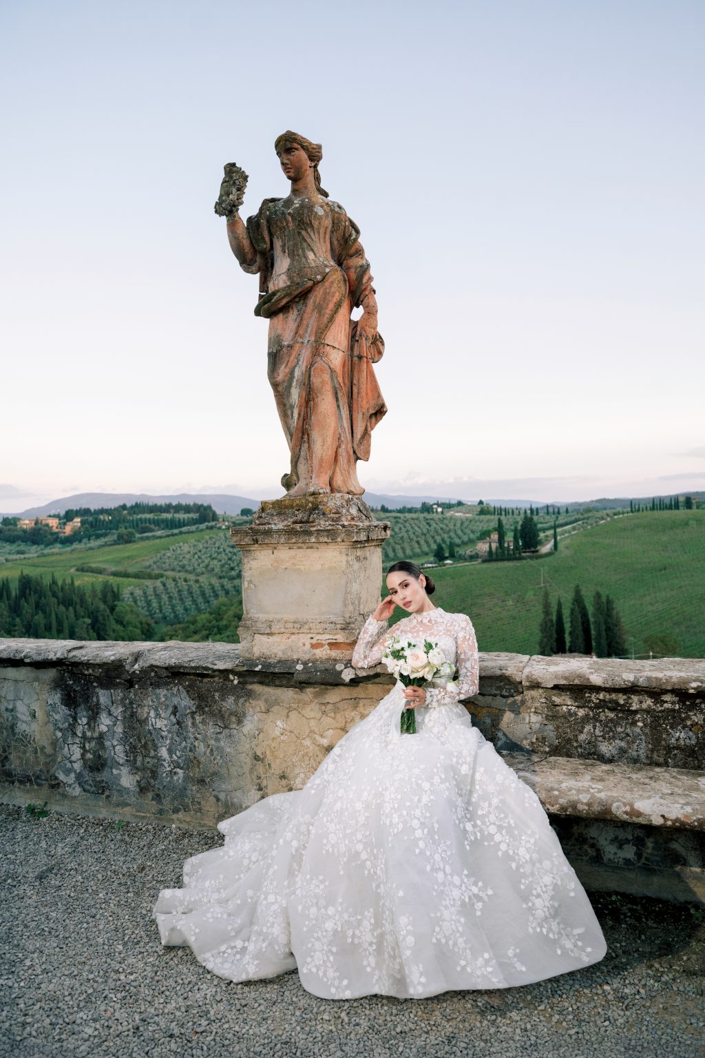 Bride beside a terracotta statue overlooking the Tuscan hills